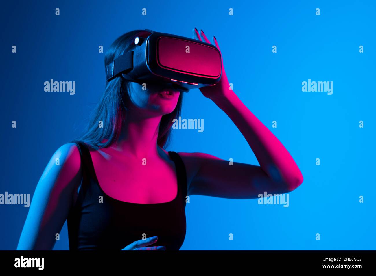 Fröhliches Mädchen mit den Händen nach oben trägt die Virtual-Reality-Brille und spielen ein Spiel in Neonlicht. Technologiekonzept der Zukunft. Metaverse Stockfoto