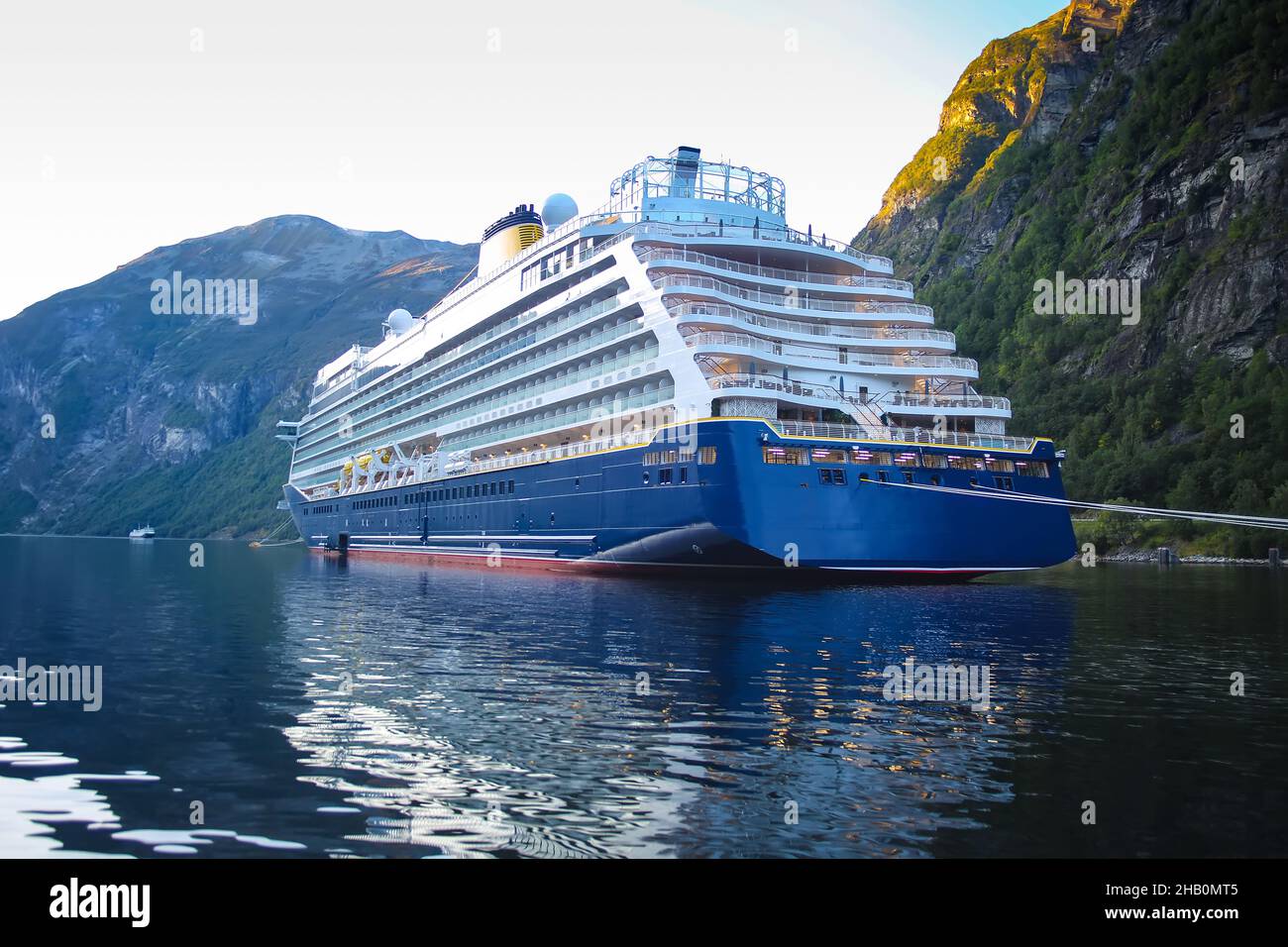 An einem schönen Sommertag steht das Schiff vor Anker. Spiegelungen der Berge im Fjord. Üppig grüne Landschaft mit Gipfeln, die über dem Wasser emporragen. Stockfoto