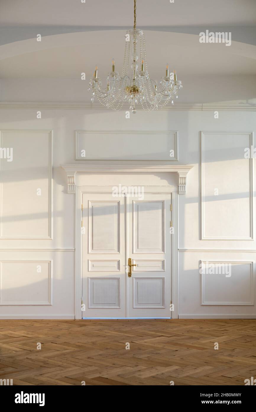 Weiße, geschlossene Türen in hellem, geräumigen, leeren Raum mit klassischem Design und Kronleuchter, der an der Wand mit Sonnenlicht hängt Stockfoto