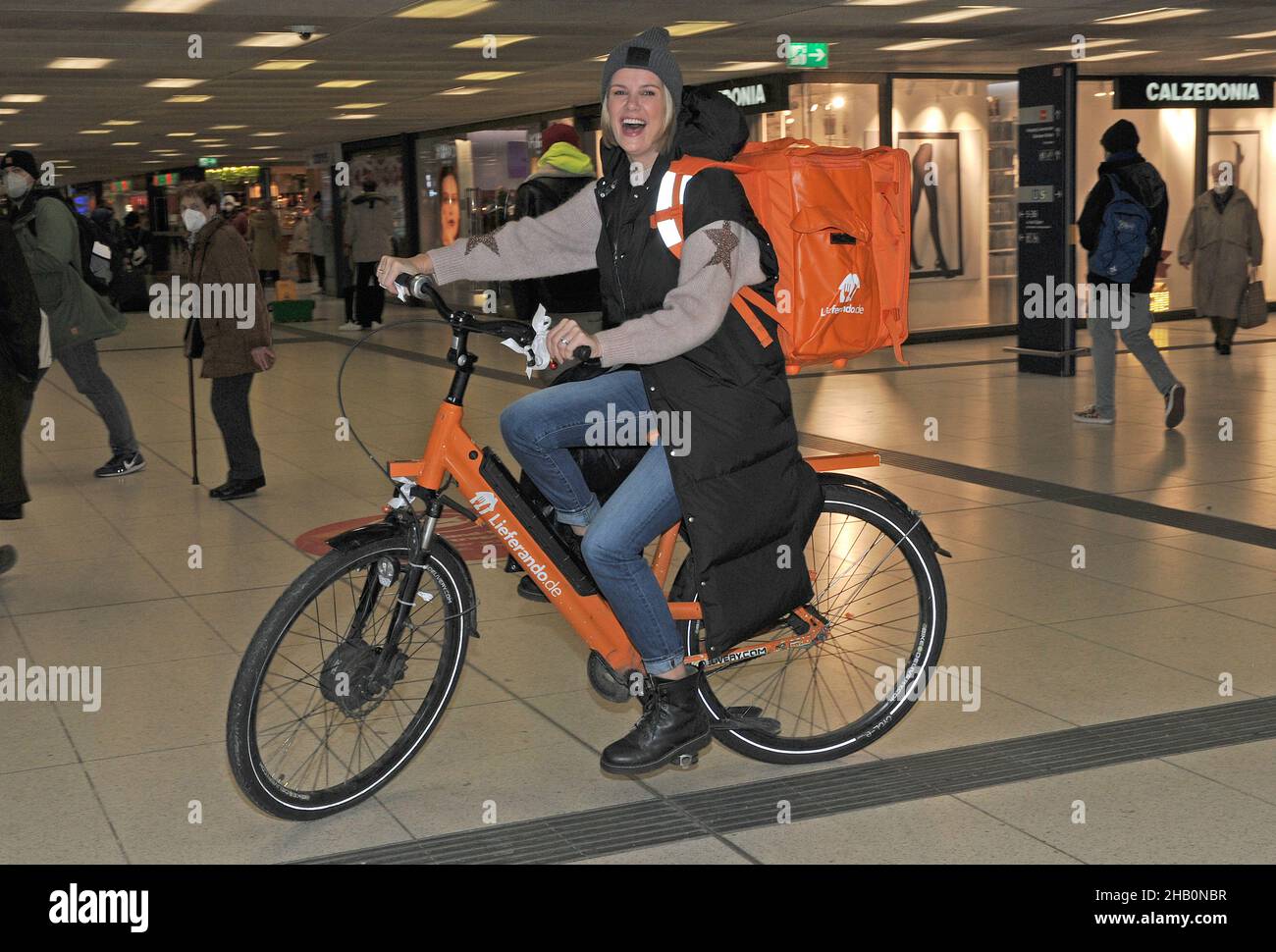 München, Deutschland. 16th Dez 2021. Model Monica Ivancan fährt bei der  Eröffnung des Lieferando Wish Tree für die Arche im Untergeschoss des  Münchner Hauptbahnhofs mit dem Fahrrad von Lieferando. Quelle: Ursula  Düren/dpa/Alamy