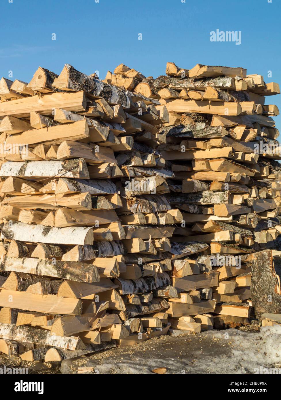 Gespitztes Brennholz, das in einem Stapel von Holzstämmen auf dem Hintergrund des blauen Himmels gebaut wurde. Stapel von Holzkeilen für den Backofen Stockfoto