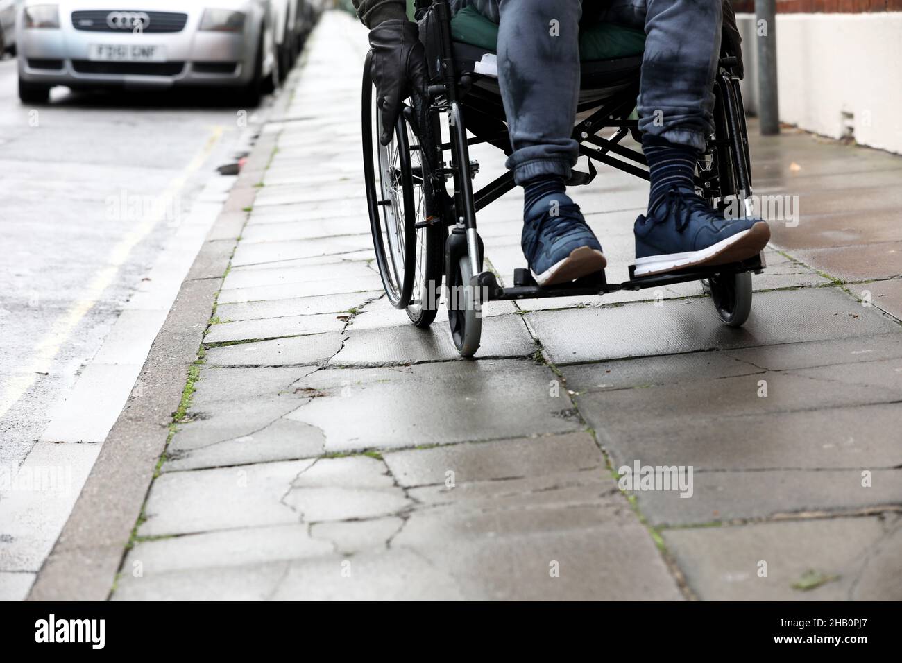 Ein Mann in einem Rollstuhl, der ihn in London, Großbritannien, auf einem unebenen Weg benutzte. Stockfoto
