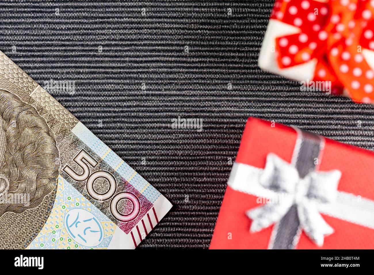 Polnischer 500PLN-Banknote mit Geschenken auf grauem Hintergrund. Kleine Kisten mit Schleifen. Foto aufgenommen unter künstlichem, weichem Licht Stockfoto