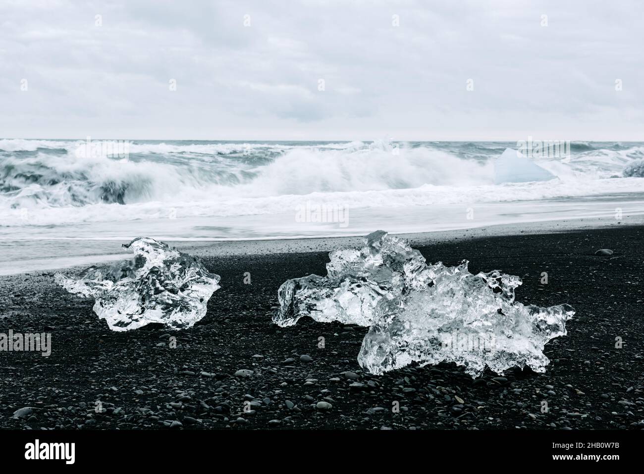 Eisbergstücke am Black Diamond Strand in der Nähe der Jokulsarlon Lagune, Island. Wellen des Atlantiks und wolkige Himmel auf dem Hintergrund. Landschaftsfotografie Stockfoto