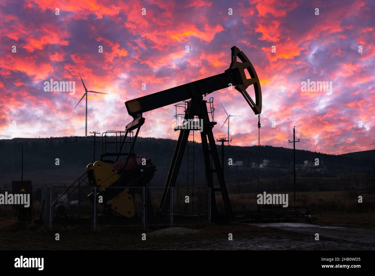 Ölpumpe und Windturbinen gegen den unglaublich violetten Sonnenuntergang. Industriekonzept Stockfoto