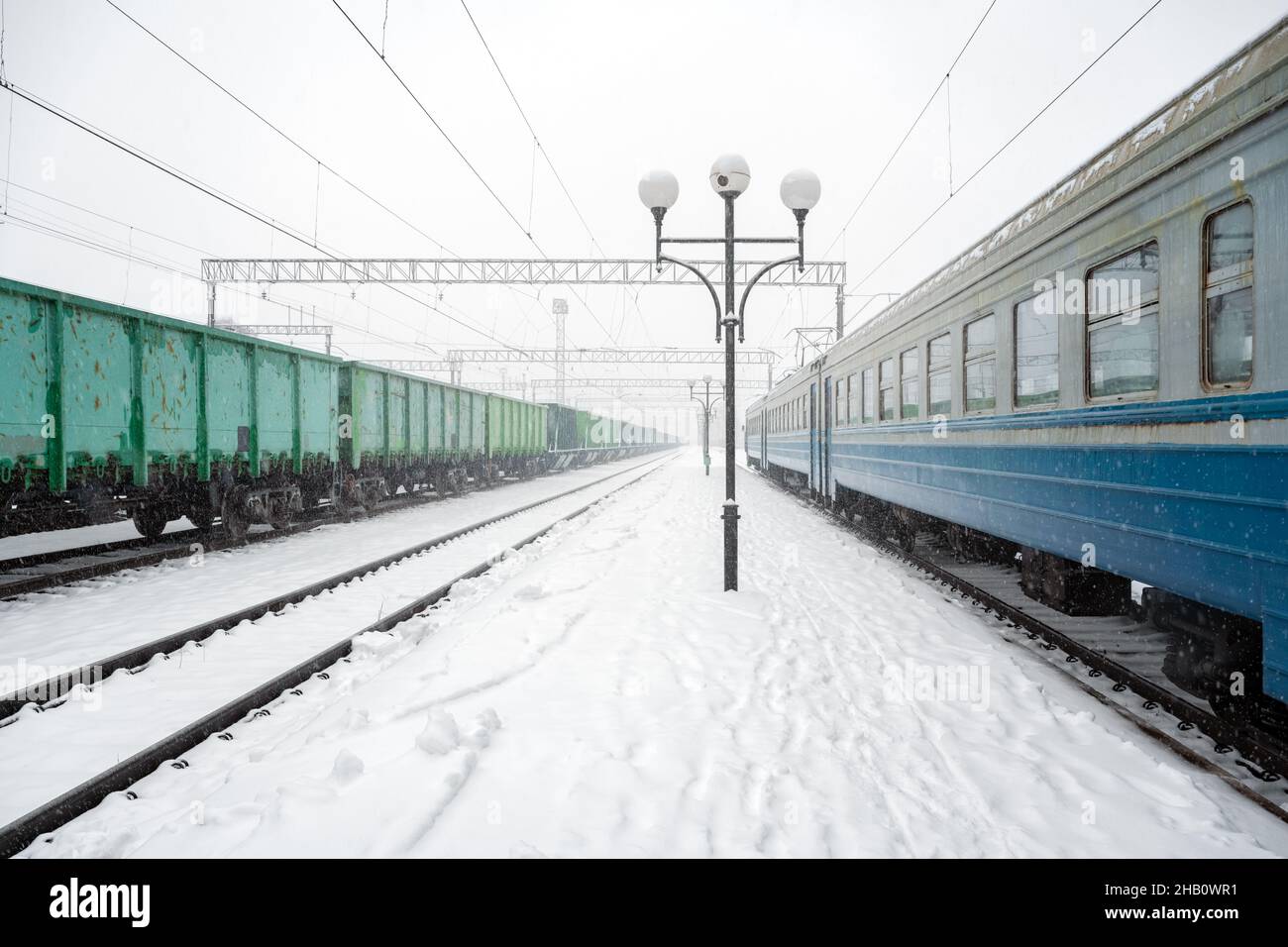 Bahnhof peron im Winter von Schnee bedeckt. Personenzug und Güterwagen auf verschneiten Eisenbahnen. Ukraine, Europa Stockfoto