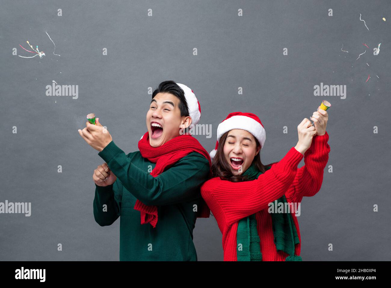Glücklich aufgeregt asiatische paar ziehen Party Poppers feiern Weihnachten in isolierten Studio grauen Hintergrund Stockfoto