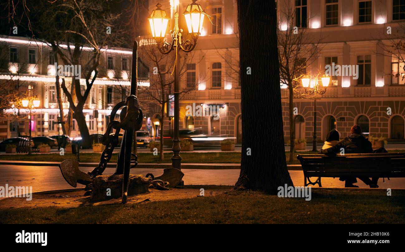 Szene der Abendstadt mit einem Paar auf einer Bank und einem Schiffsankerdenkmal in der Nähe des Operntheaters in Odessa Ukraine. Stockfoto