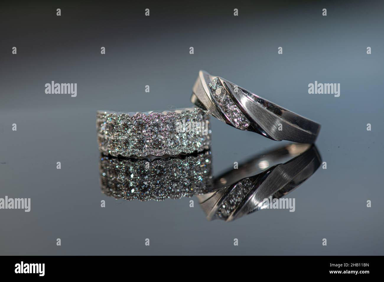 Weißes Gold Bräutigam Hochzeitsband auf Bräute Ring Diamanten auf Glas reflektierende Oberfläche Stockfoto