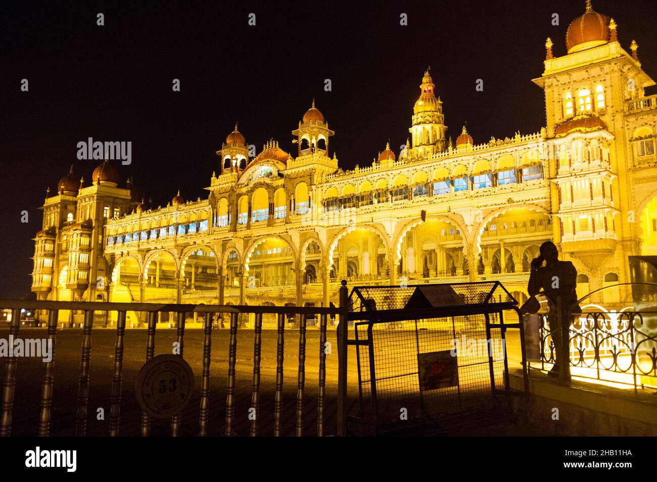 Mysore, Karnataka, Indien : Ein Wachmann steht nachts vor dem beleuchteten Mysore Maharaja Palast. Stockfoto