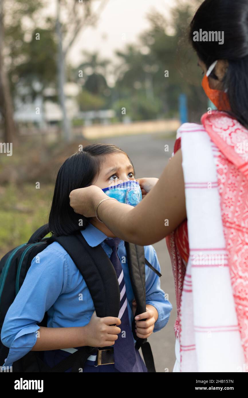 Ein indisches Schulkind, das nach einer Pandemie wieder zur Schule geht, wobei ihre Mutter Nasenmaskenschutz trägt Stockfoto