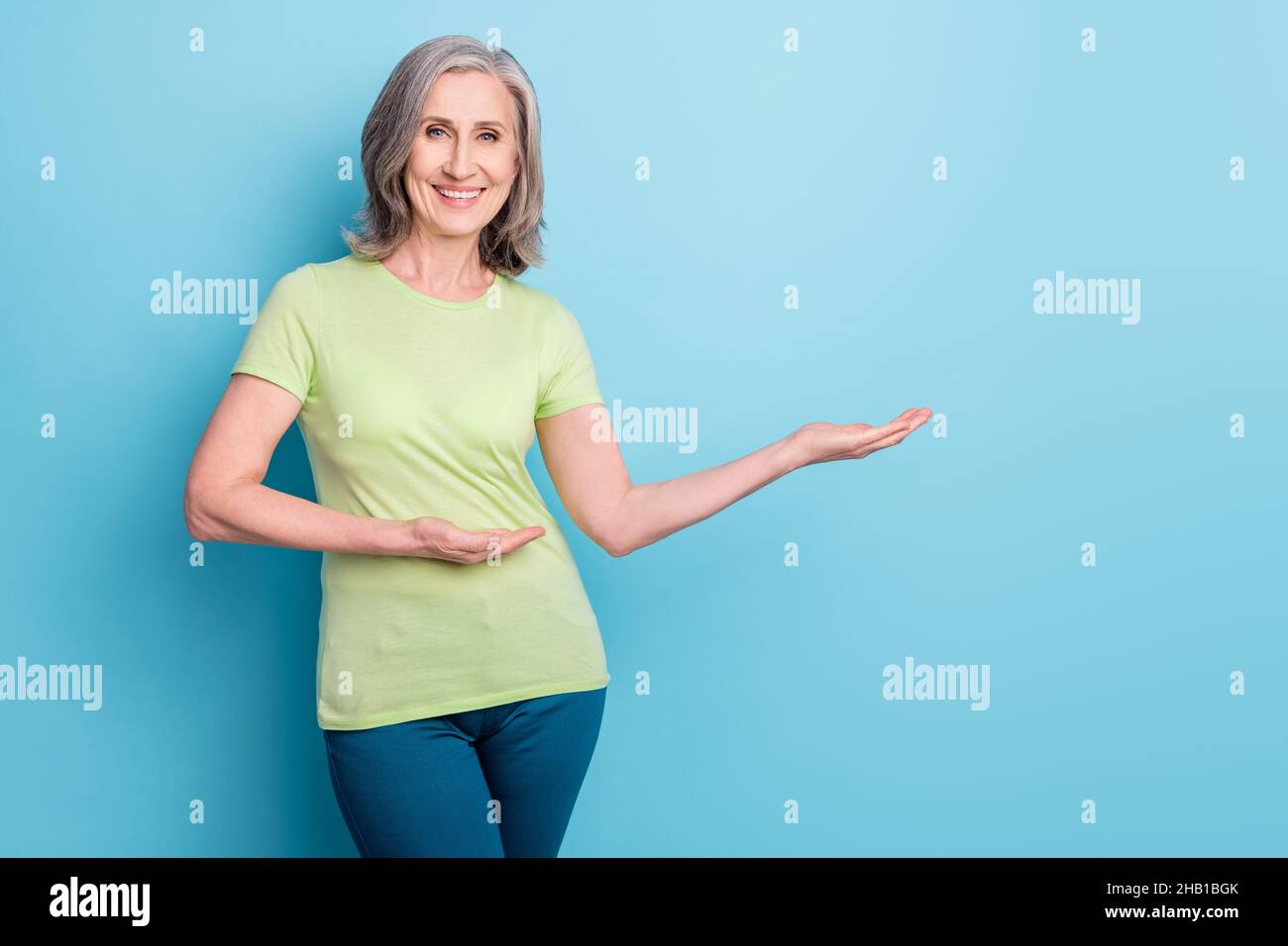 Foto von attraktiven fröhlichen alten Frau halten Hände leeren Raum entscheiden Produkt auf blauem Hintergrund isoliert Stockfoto