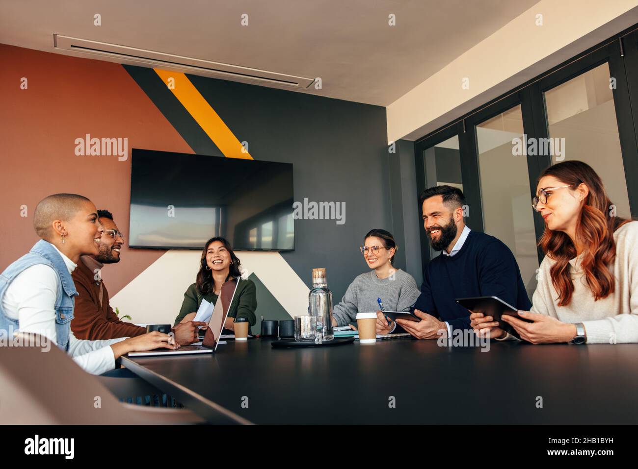 Fröhliche Geschäftsleute, die sich in einem Sitzungssaal treffen. Eine Gruppe von multiethnischen Geschäftsleuten, die während ihrer morgendlichen Besprechung fröhlich lächeln. Junge Entr Stockfoto