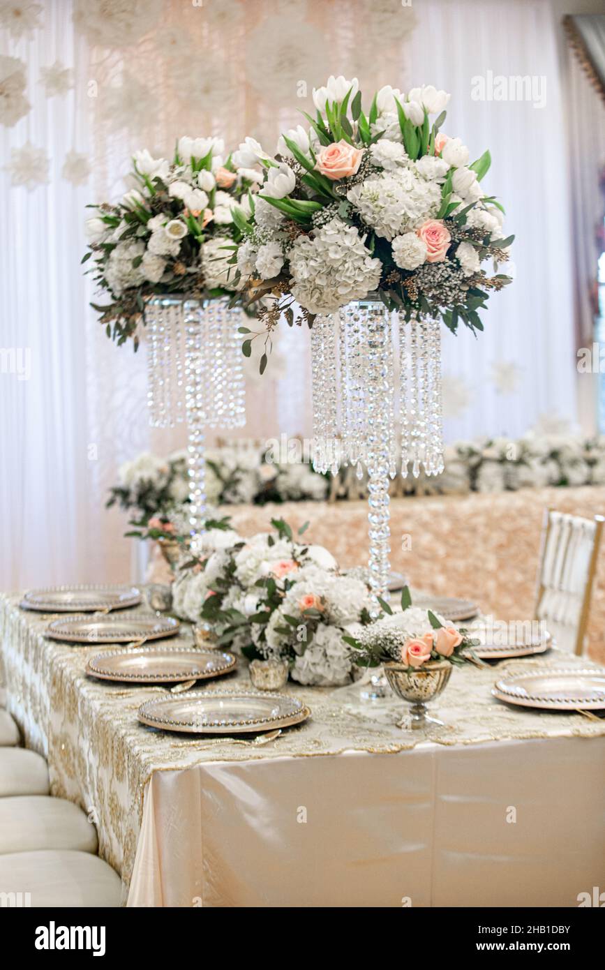 Hohe Hochzeitsempfänge mit Kristallen und Hortensien sowie weißen und rosafarbenen Blumen auf goldenem Tischgestellen Stockfoto