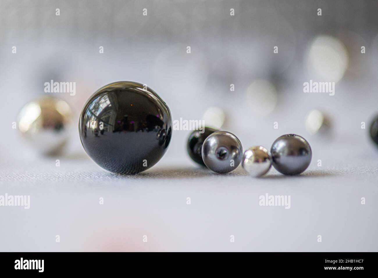 Glänzende Kugeln in verschiedenen Farben schwarz, grau, Gold in einer Gruppe auf weißer Oberfläche abstrakt Stockfoto