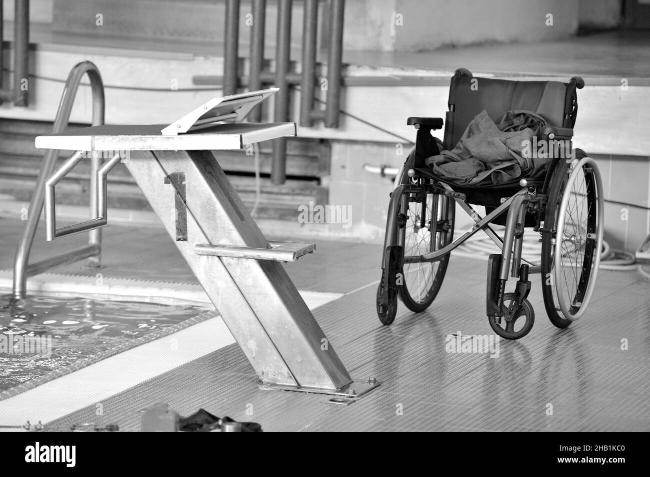 Graustufenaufnahme eines Rollstuhls an einem Sprungbrett in einem Hallenbad Stockfoto