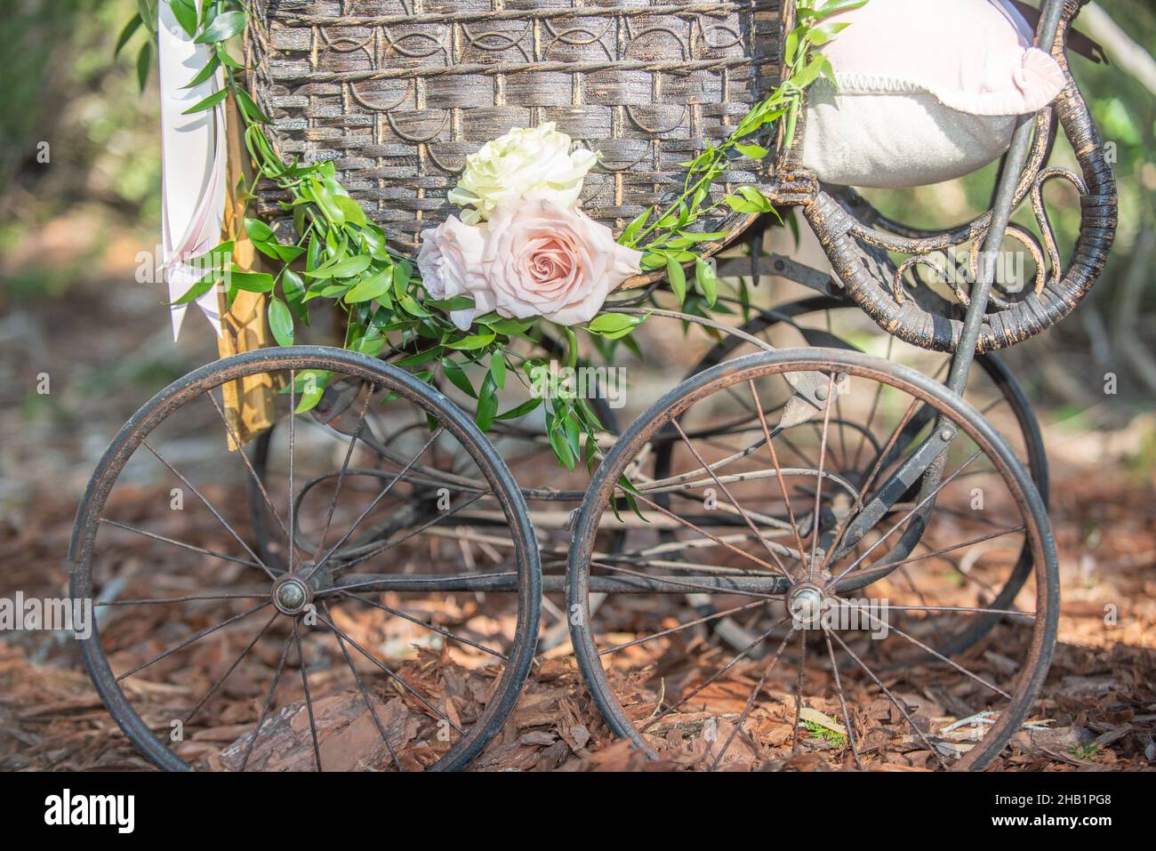 Alte verrostete Waggonradfelge an Holz als Yard-Dekor befestigt fashioned Radwagen Baby Wagen mit Webkorb dcorated mit rosa Blumen und gr Stockfoto