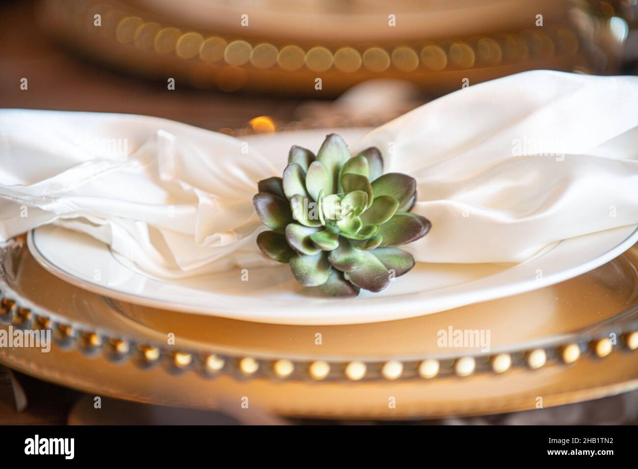 Serviette aus weißem Leinen, Blumennapkin-Ring auf goldenen Ladegeräten Stockfoto