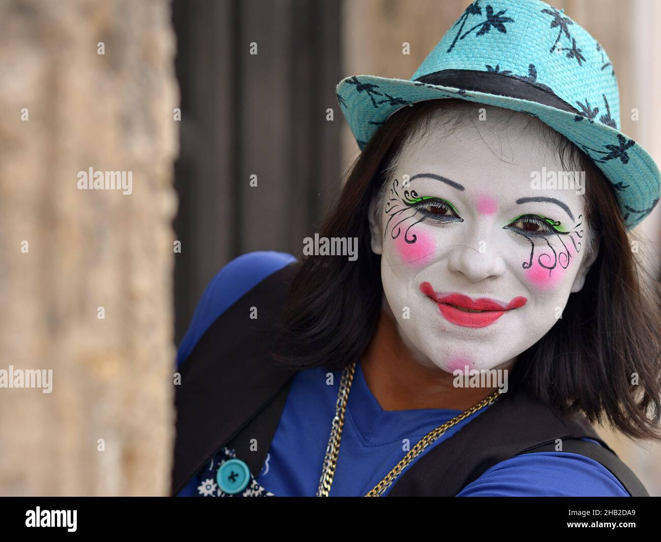 Der junge mexikanische Clown mit weißem Clown-Make-up blickt am Tag der Toten (Día de los Muertos) um die Wandecke und schaut den Zuschauer an. Stockfoto