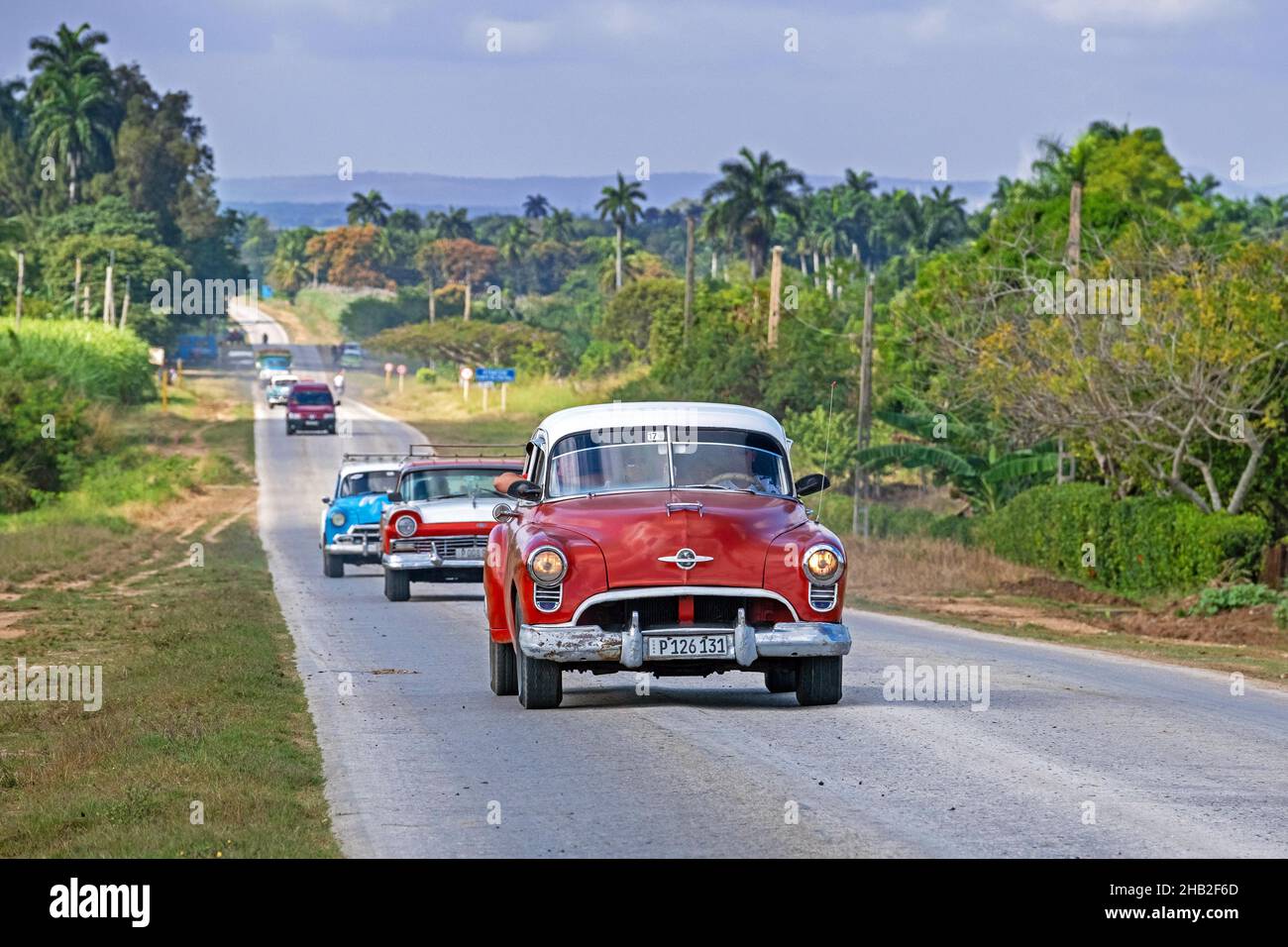 Klassische amerikanische Autos fahren entlang der Carretera Central / CC / Central Road, West-Ost-Autobahn in der Provinz Sancti Spíritus auf der Insel Kuba Stockfoto