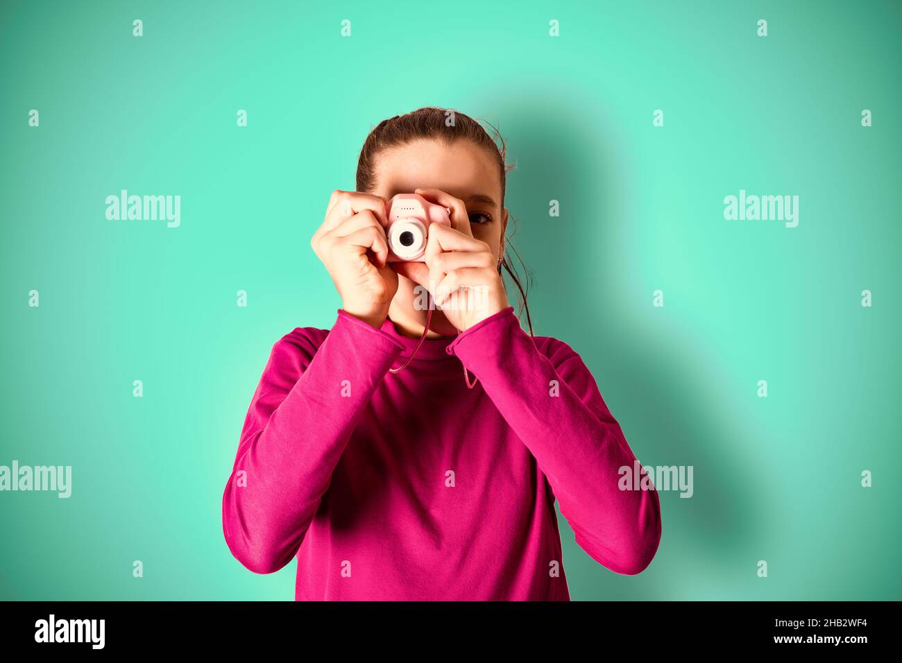 Kleines Mädchen, das Bild mit Spielzeug-Fotokamera auf cyanfarbenem Hintergrund Stockfoto