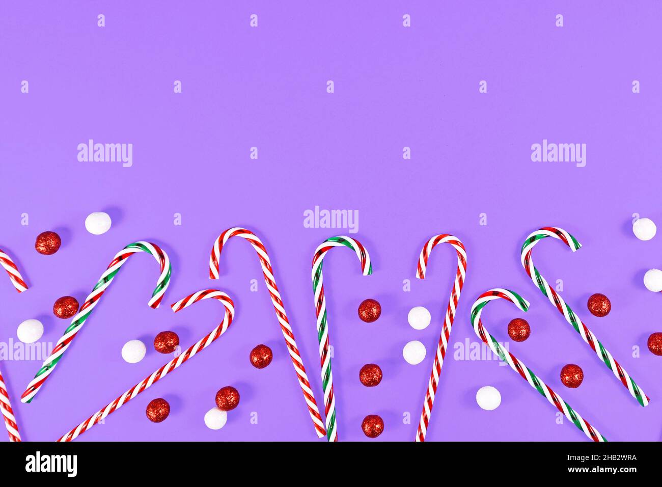 Weihnachten Süßigkeiten Stöcke und Ornament Kugeln unten auf lila Hintergrund mit Kopieplatz Stockfoto