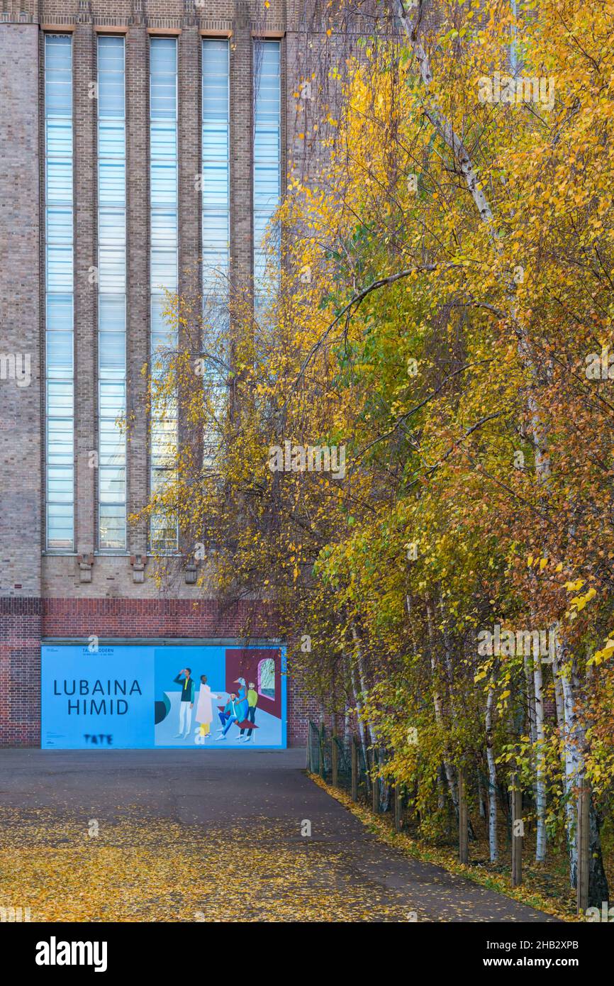 Bäume mit Herbstfarben und Plakat-Banner Werbetafel Werbung Lubaina Himid Ausstellung vor der Tate Modern, London UK im Dezember Stockfoto