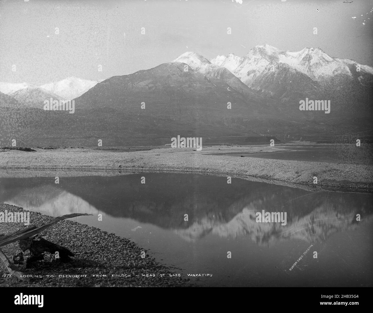 Blick auf Glenorchy von Kinloch, Leiter des Lake Wakatipu, Burton Brothers Studio, Fotostudio, 1883, Neuseeland, Schwarzweiß-Fotografie, Blick auf schneebedeckte Berge über einem kleinen Gewässer, wobei sich die Berge in diesem Wasser spiegeln. Ein Stück Treibholz dringt ganz unten links in den Rahmen ein Stockfoto