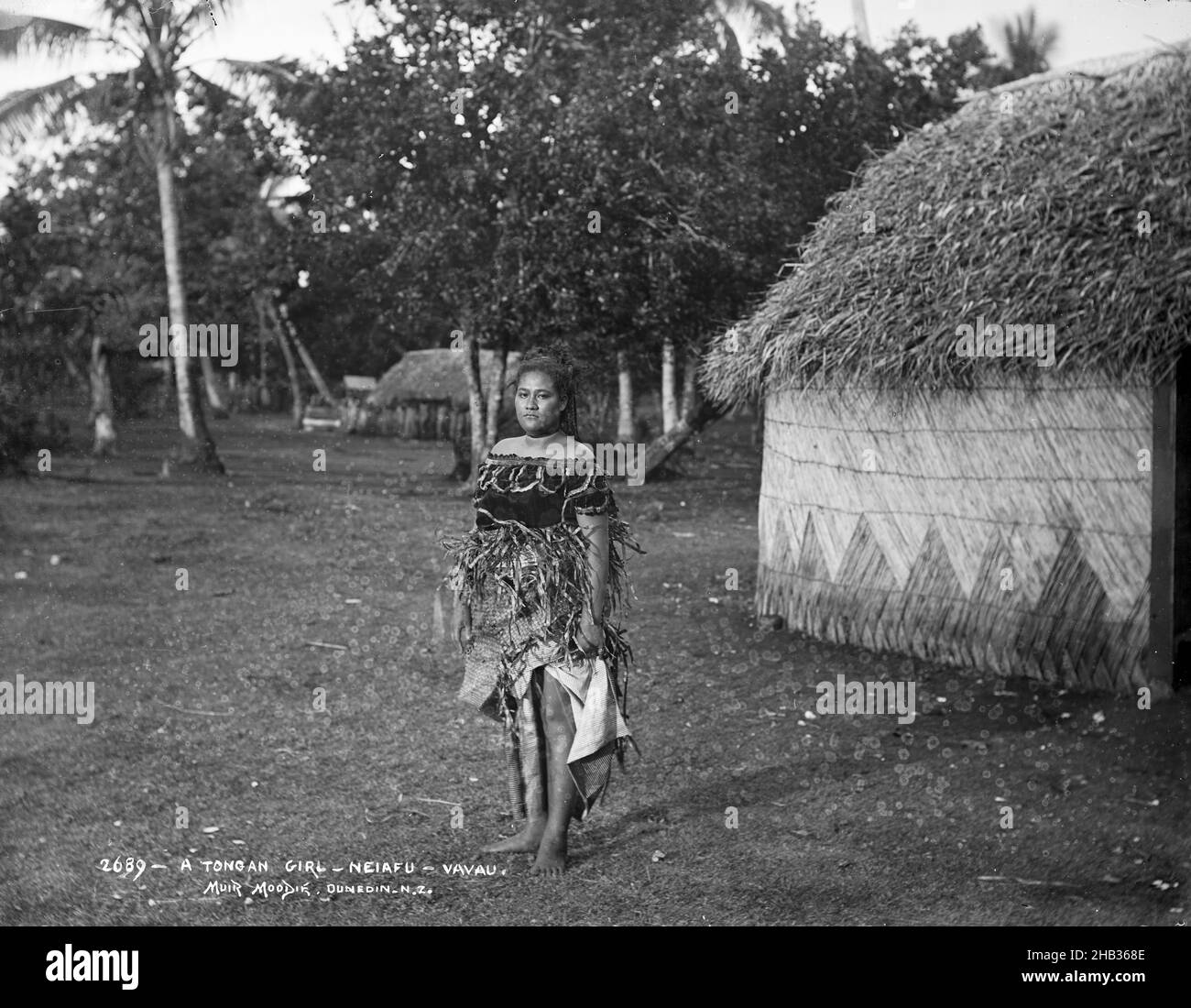 A Tongan Girl, Neiafu, Vavau, Burton Brothers Studio, Fotostudio, Juli 1884, Neuseeland, Schwarz-Weiß-Fotografie, Eine Tongan-Frau, die auf einer Lichtung vor einem Fale steht, mit gewobenem Dach und Wänden. Ein weiteres Fale ist im Hintergrund. Hohe Bäume sind im Hintergrund Stockfoto