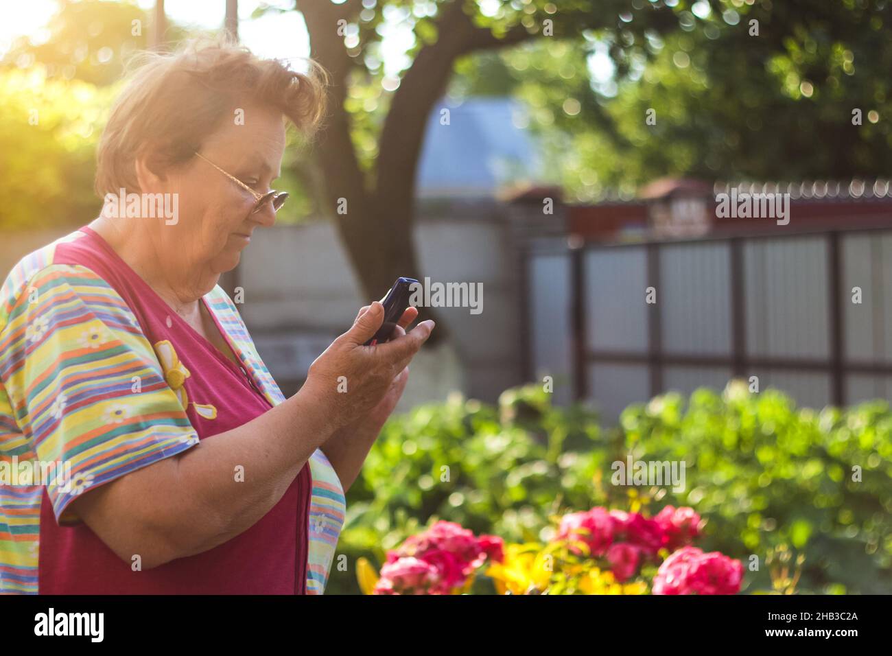 Eine 65-jährige Frau schaut auf das Telefon im Hof Oma lernt, wie man das Telefon zu verwenden .Porträt von gut aussehenden reifen Frau mit Smart pho Stockfoto
