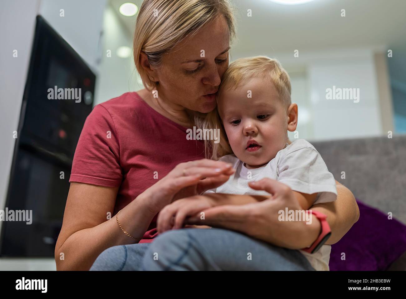 Der kleine Junge sitzt traurig auf den Knien der Mutter, seine Hand schmerzt. Stockfoto