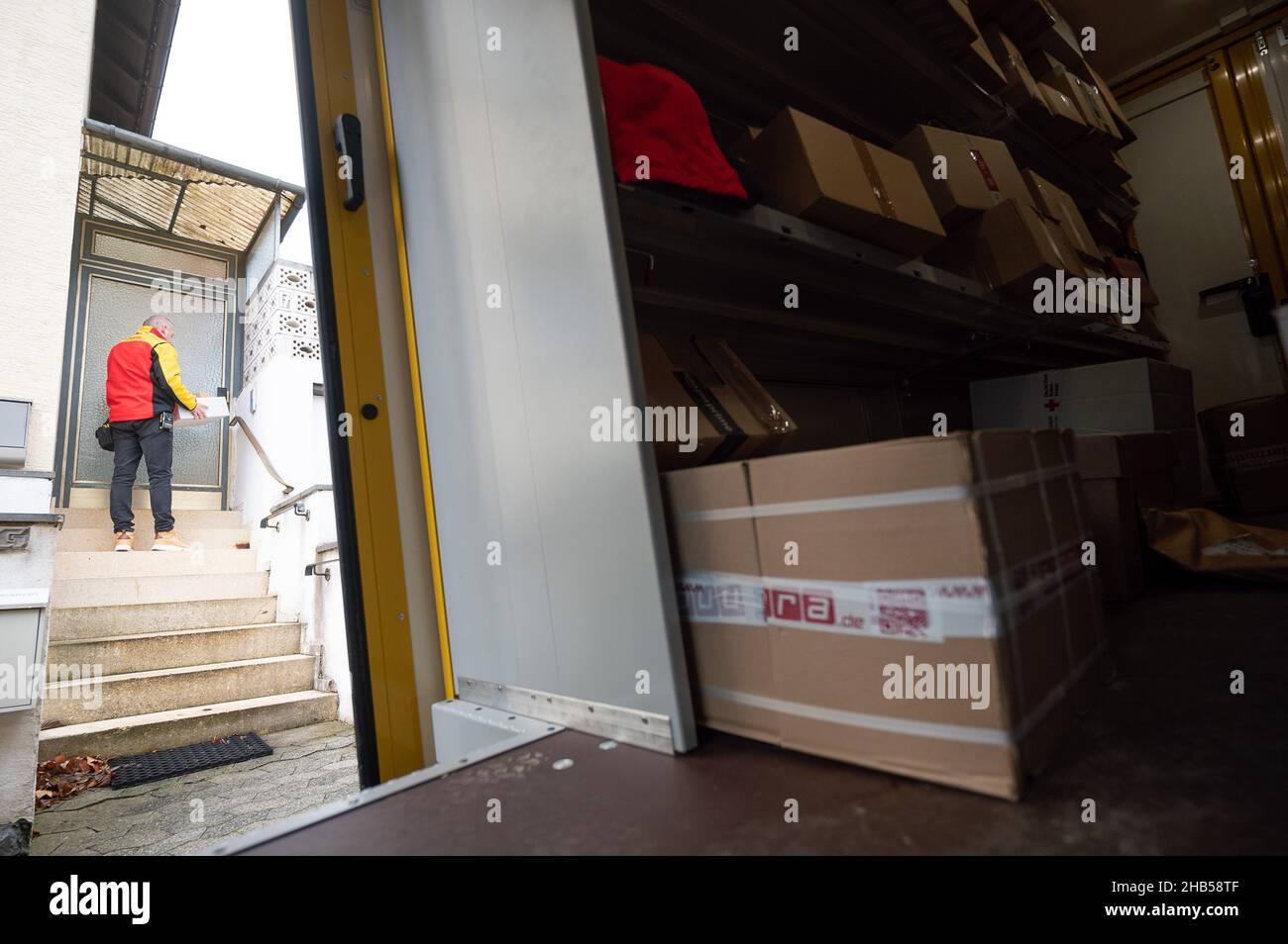 Ober Ramstadt, Deutschland. 15th Dez 2021. Ein DHL-Mitarbeiter liefert ein Paket aus, während sich noch andere Pakete in seinem Van befinden. Quelle: Sebastian Gollnow/dpa/Alamy Live News Stockfoto