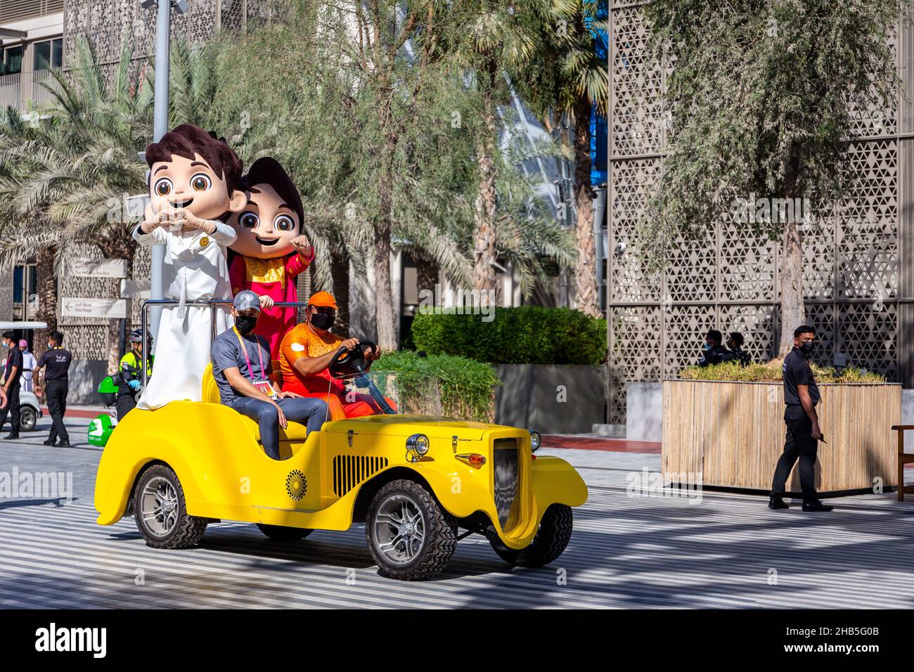 Dubai, VAE, 09.12.2021. Die Expo 2020 Dubai Maskottchen - Rashid und Latifa in traditionellen emiratischen Kostümen auf einem gelben Auto während der Expo 2020 Dubai reiten Stockfoto