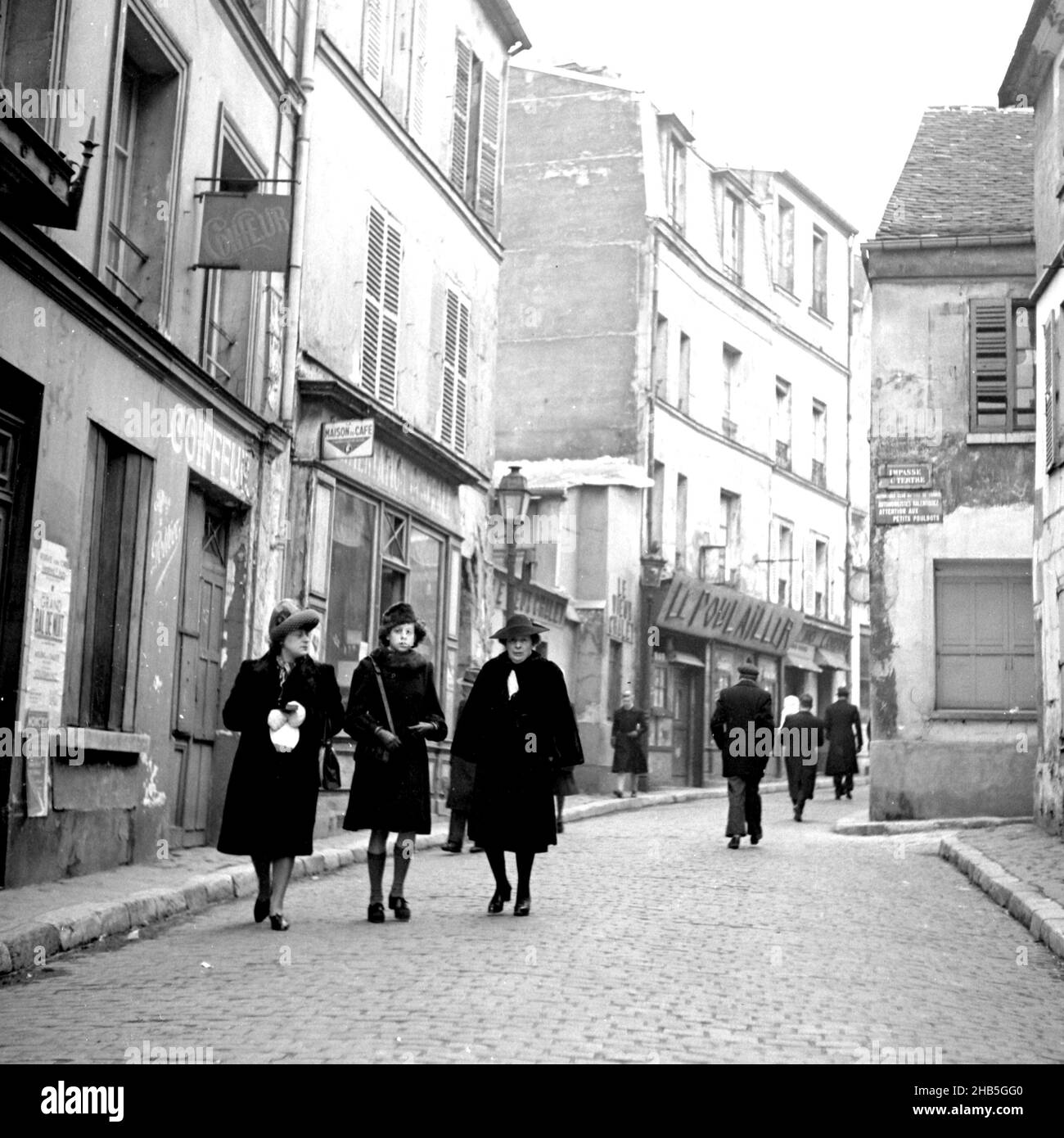 Paris Monmartre - Fußgänger auf der Rue Norvins, Winter 1945. Der Fotograf steht vor der Rue Norvins 3, um die Fußgänger in einer intimen Umgebung aufzunehmen. Nur acht Spaziergänger sind zu sehen. Die Schlüsselgruppe ist eine junge Frau, die mit zwei Frauen mittleren Alters an ihrer Seite läuft. Zwei der drei Augen der Fotograf; die junge Frau sieht alarmiert aus. Kleidung zeigt an, dass es ein kalter Tag ist. Stockfoto