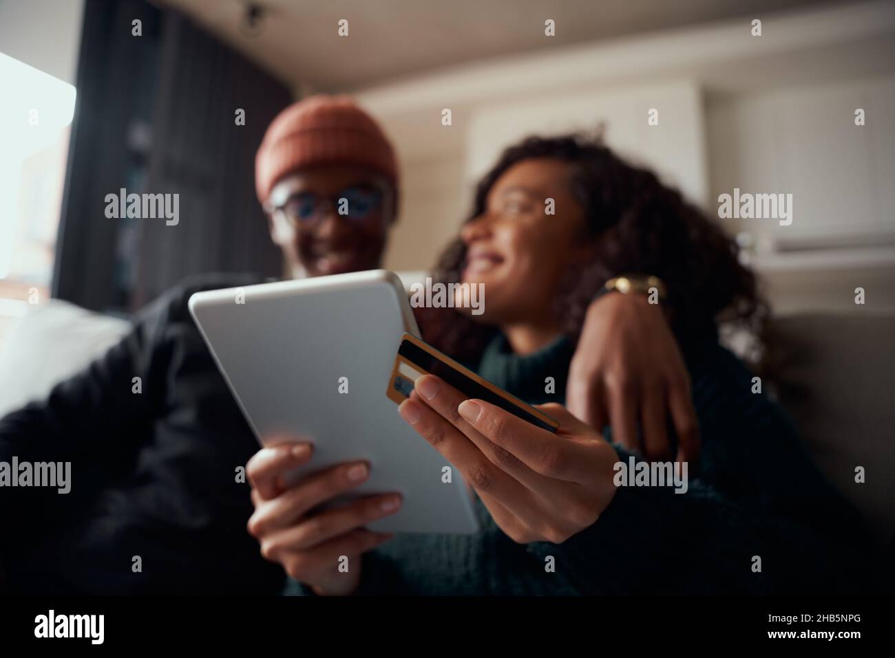 Der Online-Kauf erfolgt auf einem Tablet, das von einem multiethnischen Paar auf dem Sofa in der Lounge getätigt wurde Stockfoto