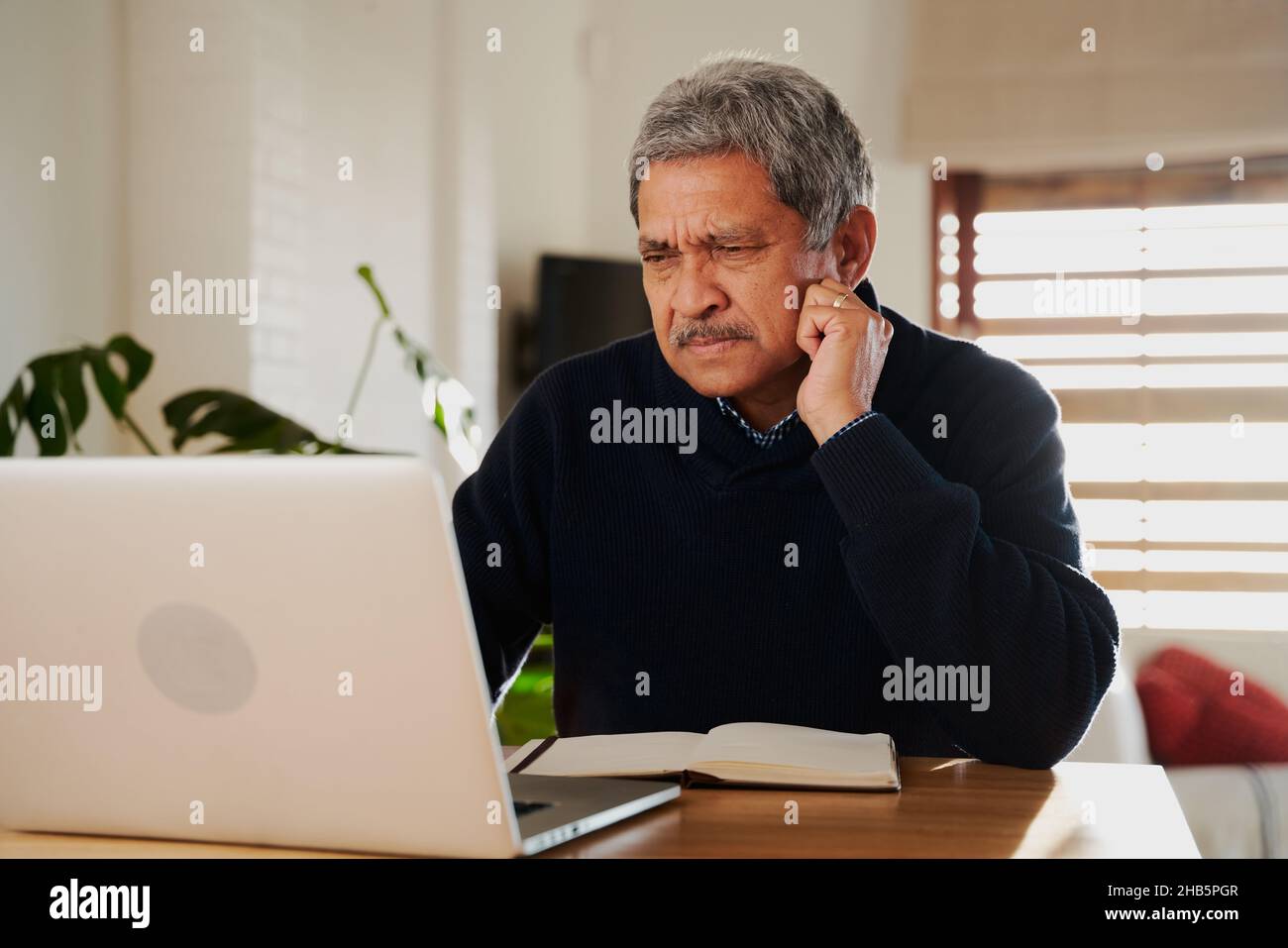 Besorgte multikulturelle ältere Menschen, die einen Laptop benutzen. Isoliert in einem modernen Zuhause, sitzend an der Küchentheke. Stockfoto