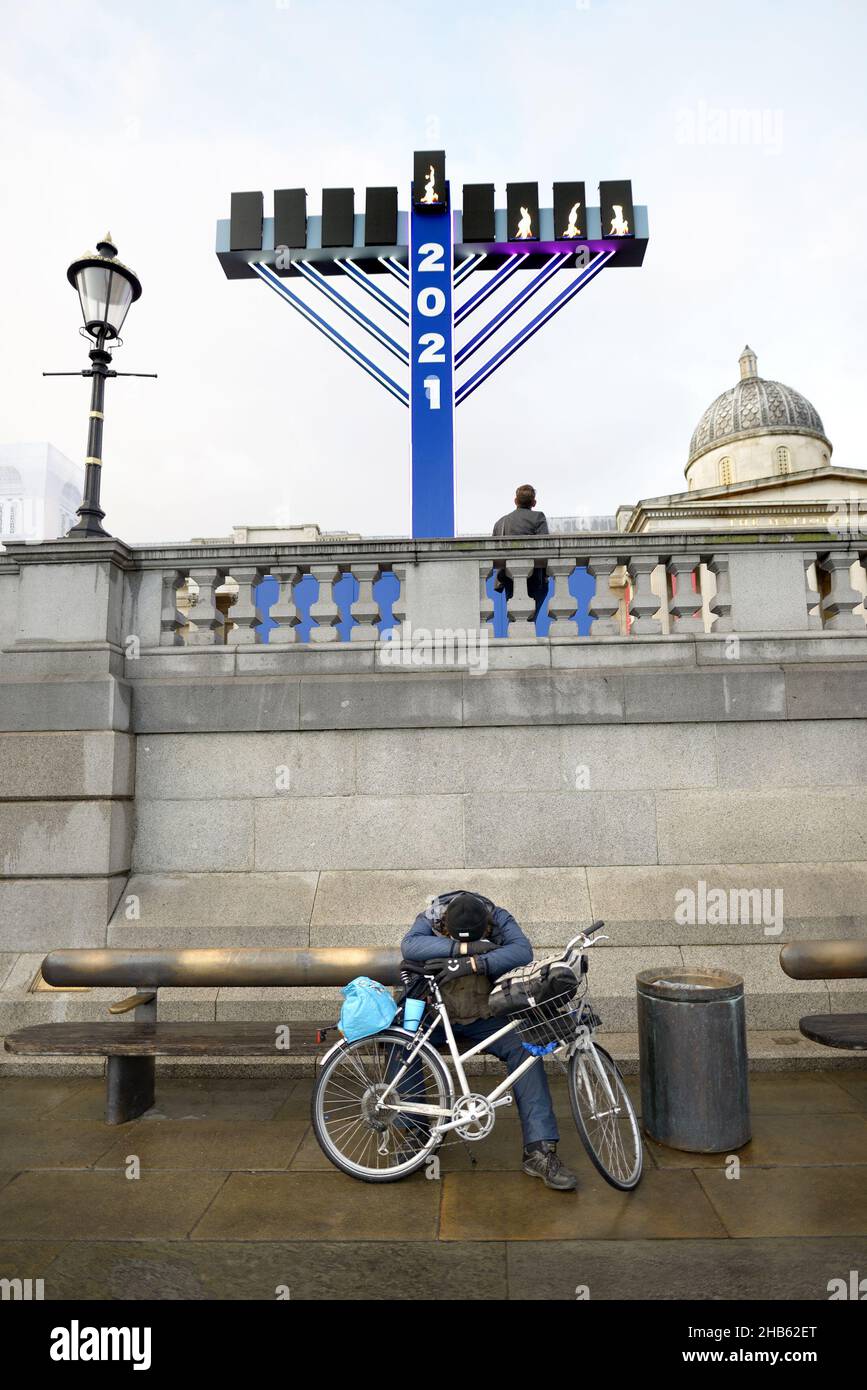 London, England, Großbritannien. Menorah auf dem Trafalgar Square, vor der Nationalgalerie, um Hanukkah 2021 zu feiern. Mann, der sich mit seinem Fahrrad ausruht Stockfoto
