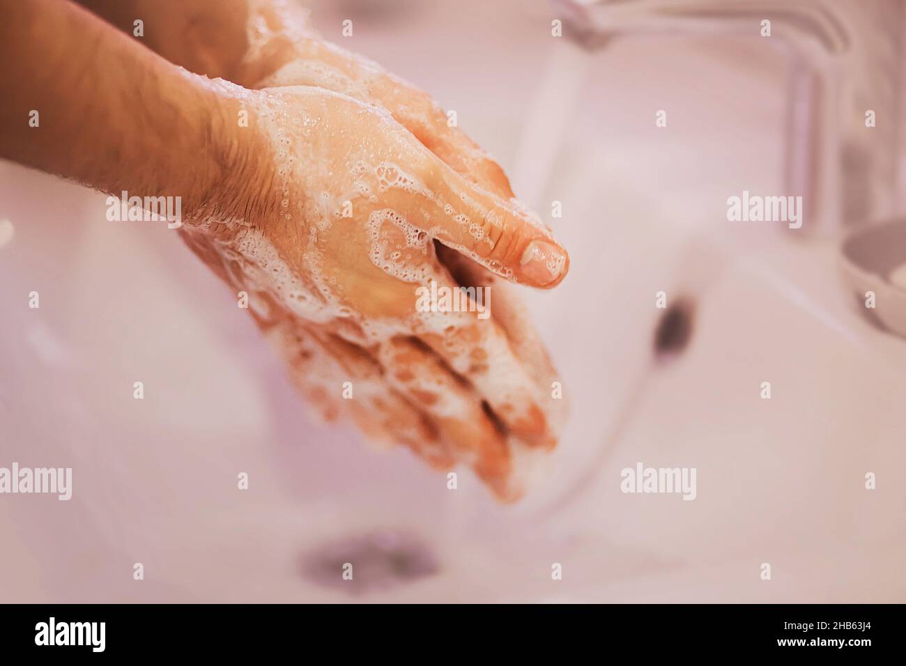 Ein Mann wäscht seine Hände vorsichtig mit Seifenlauge über einem weißen Keramikwaschbecken in der Badewanne. Sauberkeit und Hygiene. Stockfoto