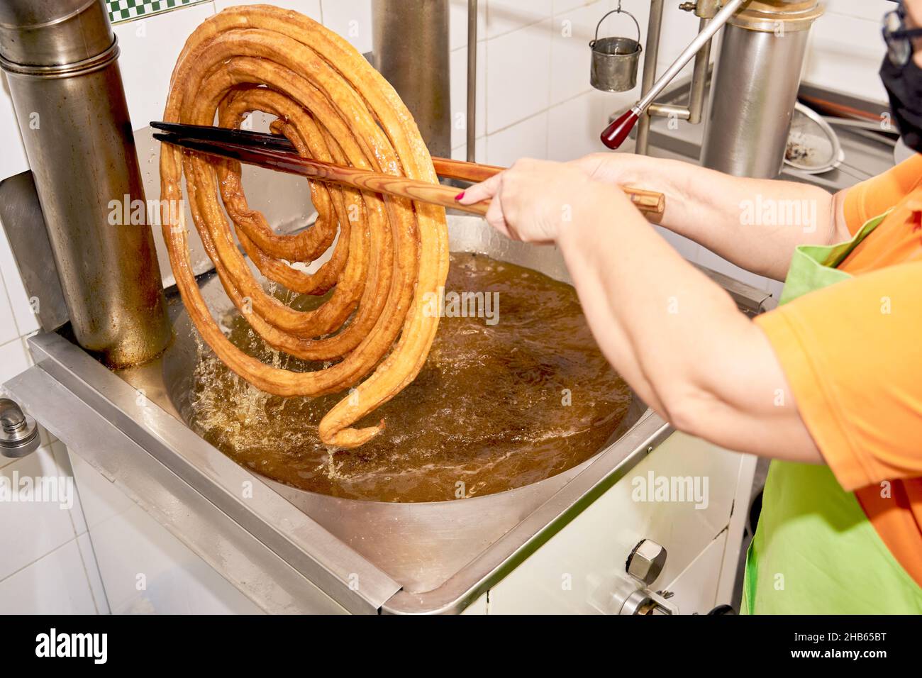 Anonymer Koch in der Schürze hält gekochten Churro-Teig mit Essstäbchen, um das Öl abzulassen. Typisch spanisches Frühstück Stockfoto