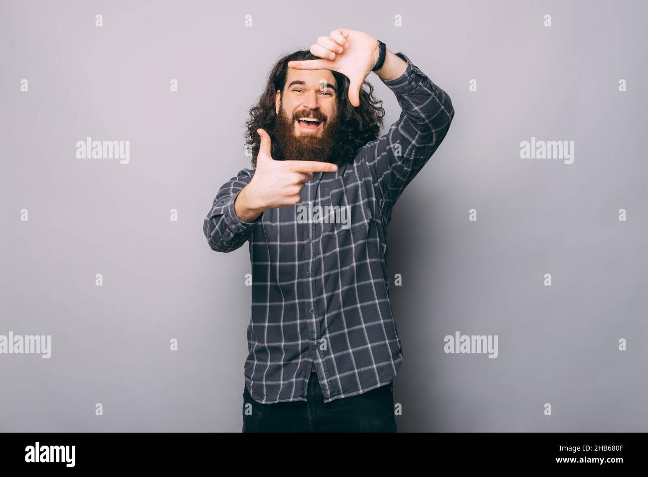 Positiver bärtiger Mann im karierten Hemd, der mit den Händen eine Frame-Geste macht und im Studio auf grauem Hintergrund auf die Kamera schaut Stockfoto