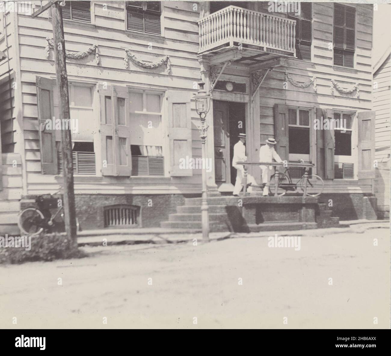 Zwei Männer vor einem Gebäude, zwei Männer mit einem Fahrrad auf der Treppe vor einem Gebäude, möglicherweise das Büro des Royal West India Mail Service (K.W.I.M.) in Paramaribo, 1911. Teil des Fotoalbums der Familie Boom-Gonggrijp in Suriname und Curaçao., Andries Augustus Boom, anonym, Paramaribo, 1911, Fotografischer Träger, Höhe 85 mm × Breite 102 mm Stockfoto