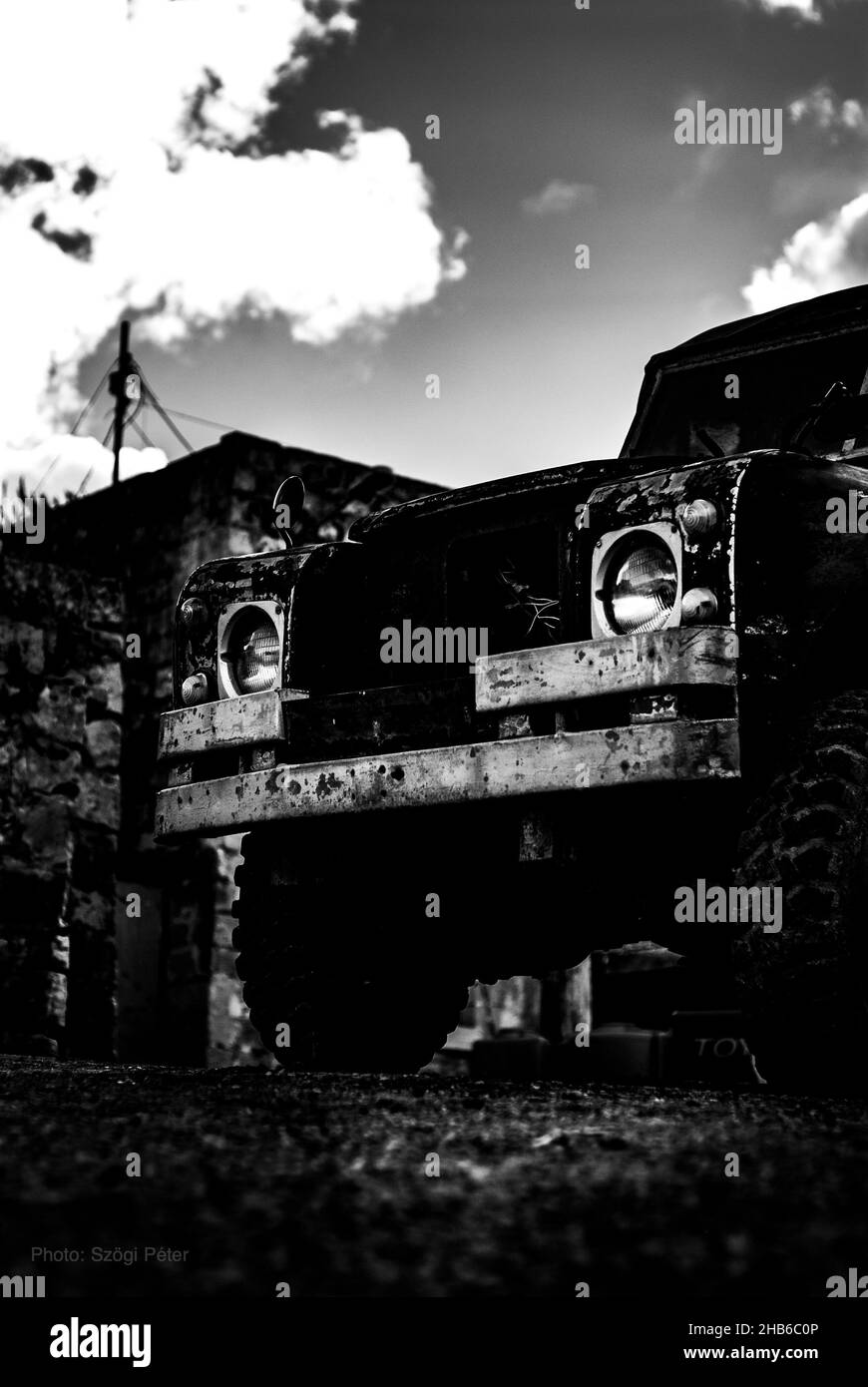 Vertikale Aufnahme eines Autos, das auf einem Feld unter dem wolkigen Himmel in Graustufen geparkt ist Stockfoto