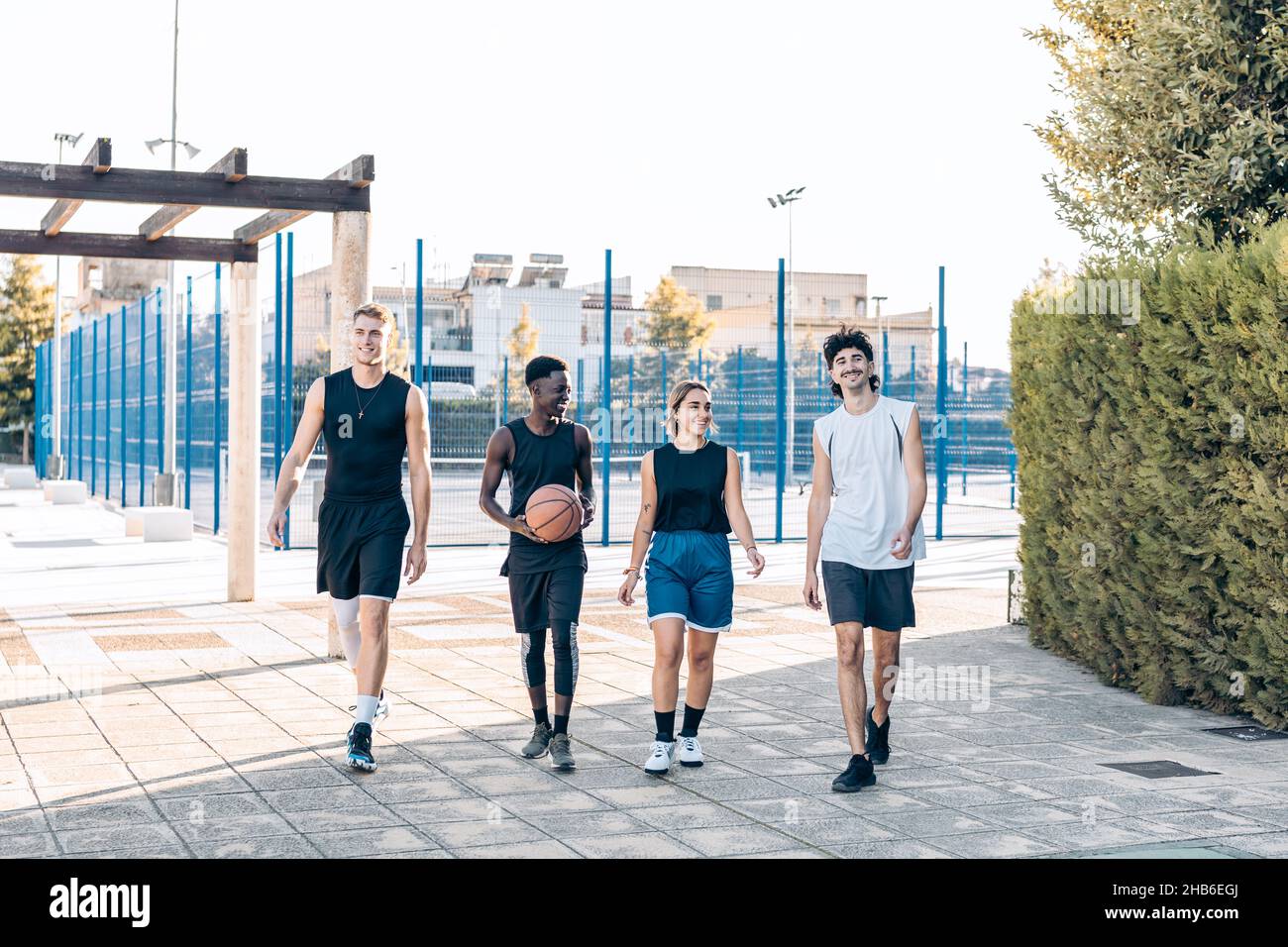 Vier Freunde verschiedener Ethnien, die vor einem Basketballplatz spazieren Stockfoto