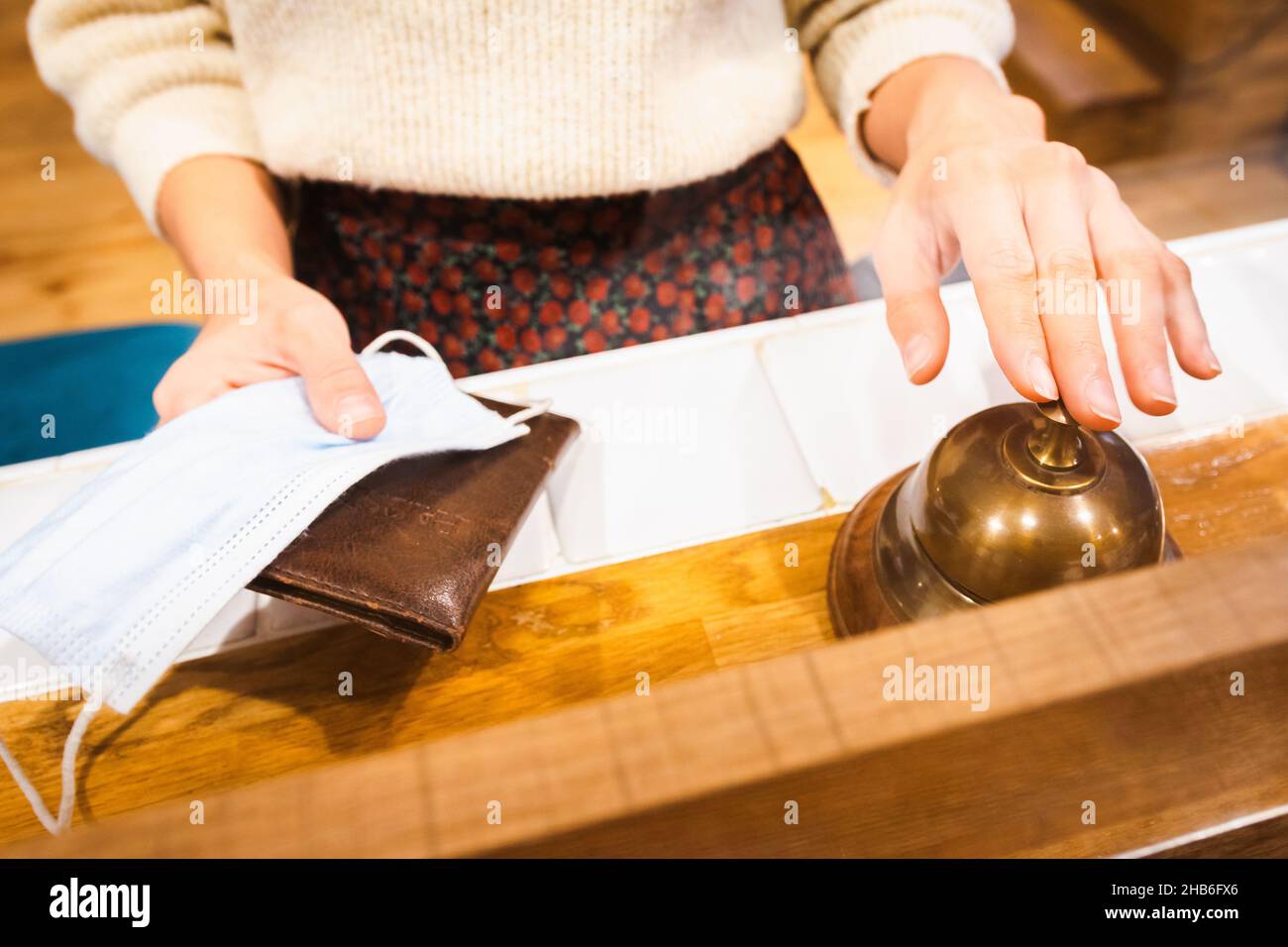 Weibliche Finger drücken die Klingel mit Pass und Gesicht auf die Hände der Rezeption im Hotel. Reisesicherheit und Einschränkungen während der Corona-Pandemie.2020 Stockfoto