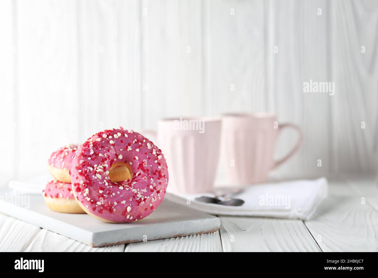 Donuts mit rosa Glasur und farbigem Karamellpulver auf weißem Holzgrund. Stockfoto
