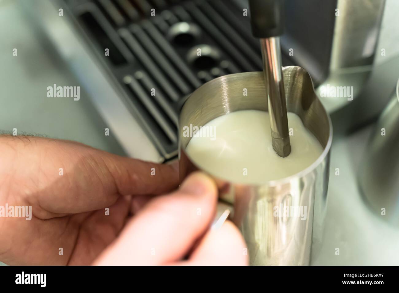 Ein Mann schäumt Milch für einen Cappuccino in einem Krug auf. Stockfoto