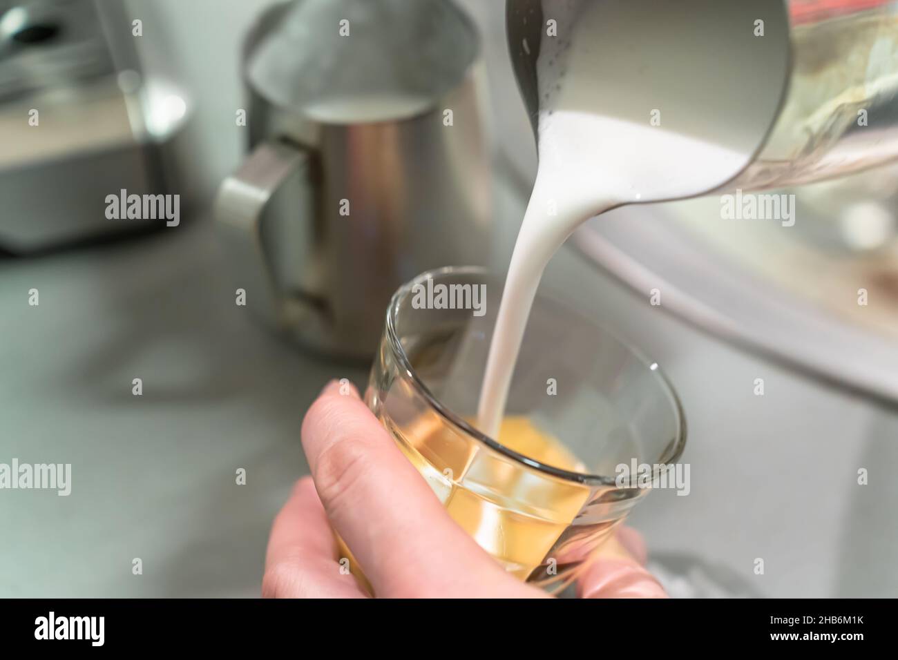 Der Barista gießt Milchschaum in ein Espressoglas. Stockfoto