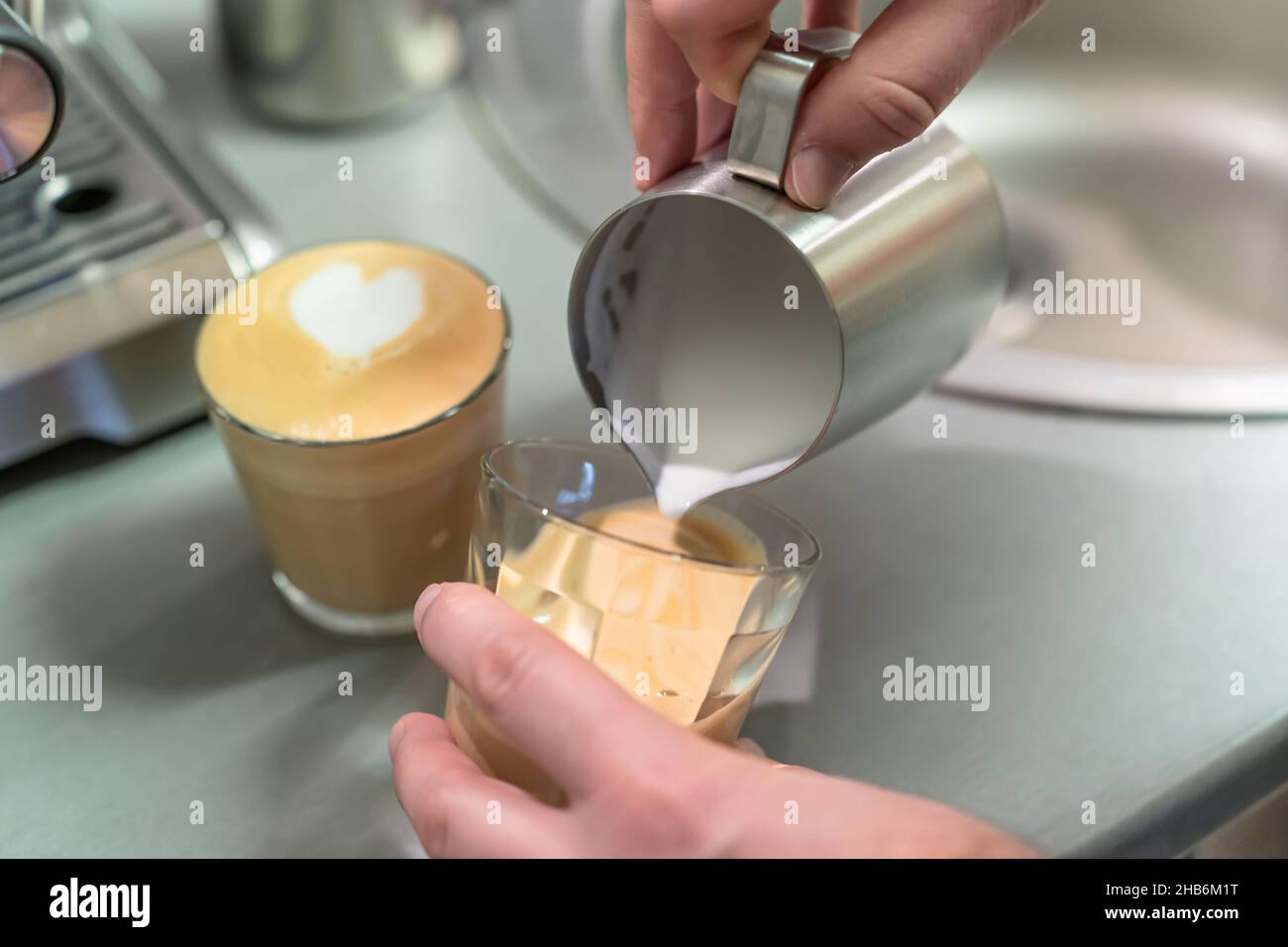 Der Barista bereitet Cappuccino zu, gießt geschlagene Milch in ein Glas Espresso. Stockfoto
