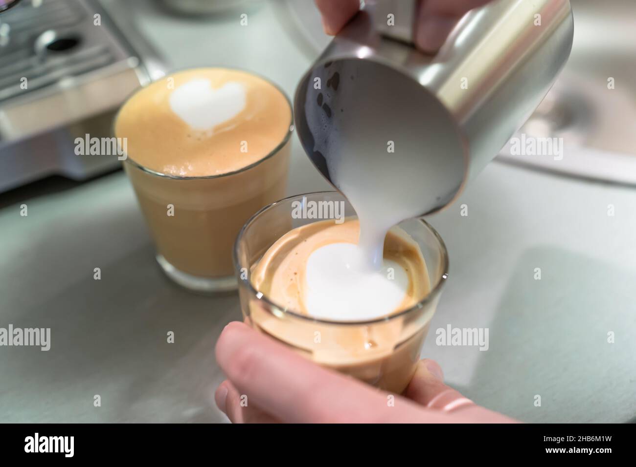 Ein Mann kocht zu Hause Cappuccino, gießt Milch aus dem Krug in ein Glas. Stockfoto