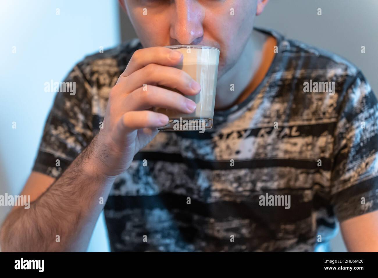 Ein Mann trinkt Cappuccino aus einem Glas, das zu Hause sitzt. Stockfoto